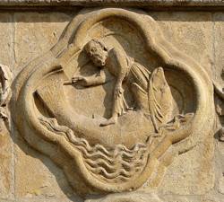 A carving of the Biblical story Jonah and the whale in light brown stone.