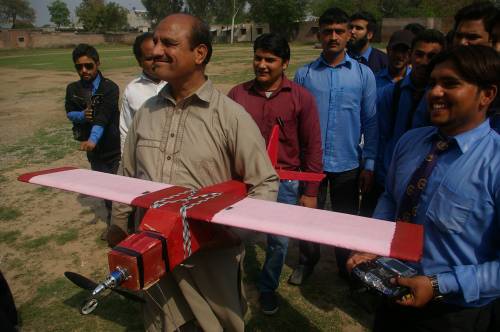 Electronics professor with students proudly showing their project, a remote control airplane