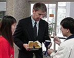 Photo of a man holding Communion bread and a cup and two other people.