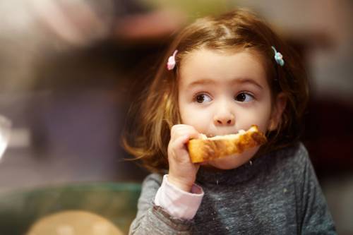 Little girl eating a piece of bread.