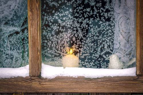 Looking inside a house through a frosty window with a candle burning on the window sill