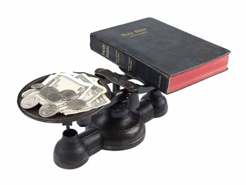 An old cast balance scale on white background balancing money versus a bible.