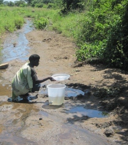 A woman taking water from a scoop hole just next to the stream which is the water source for the IDP camp.