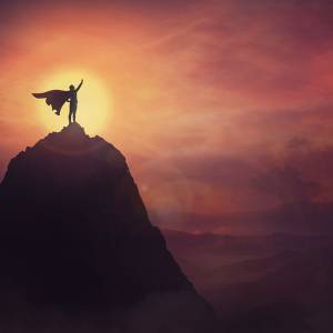 Image of "superman" type figure with a cape standing on top of a mountain