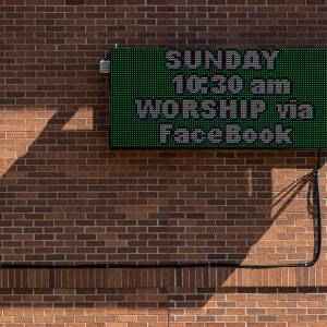Photo of outside wall of church with sign that says Sunday Worship will be on FaceBook