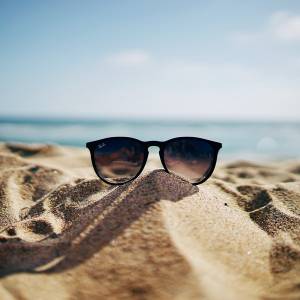 Pair of sunglasses resting on the sand at the beach.