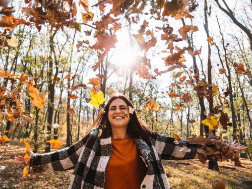 Smiling woman with arms outstretched as leaves are blowing all around her