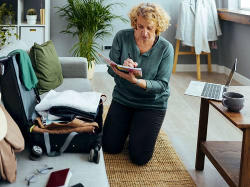 Woman packing her suitcase and checking off packed items on her list