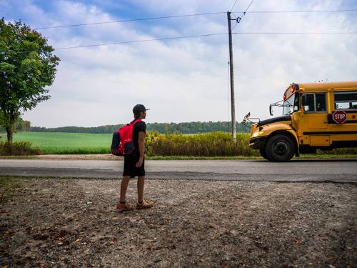 Child of color waits for a school bus in a rural area.