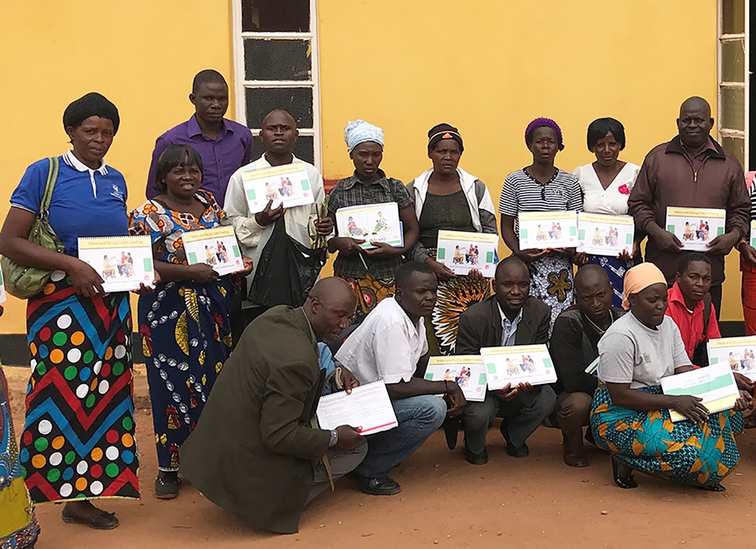 Nutrition training participants with their training manuals; the man wearing a white shirt standing in front of the window can be seen holding his chaya cuttings.