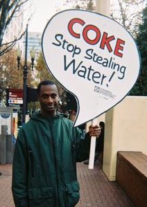Man holding sign "Coke, Stop Stealing Water!"