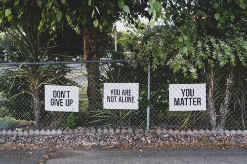 Signs on a chainlink fense in front of some trees. The signs say "Don't Give Up" "You are not alone" and "You matter."
