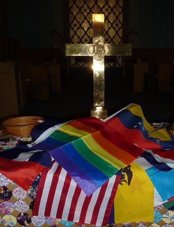 At Magdalena's previous parish, a rainbow flag celebrating LGBTQ identity joins the flags of the world during a homecoming service.
