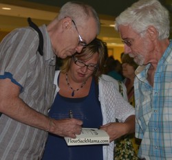 Bill McKibben signing a book with Wil Howie looking on